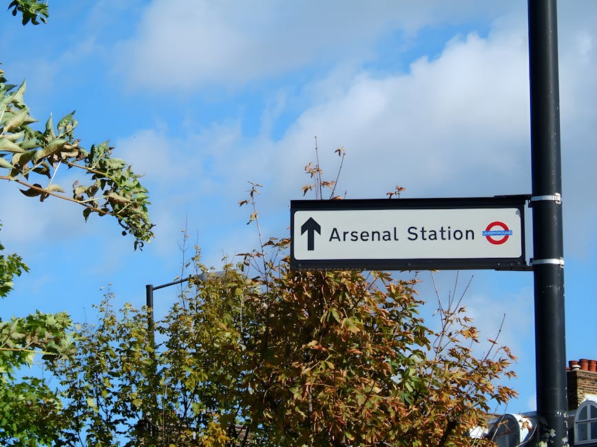 A street view outside a residential area with a small brick building surrounded by trees displaying green and autumnal foliage, under a partly cloudy sky. In the foreground, there are yellow box junct